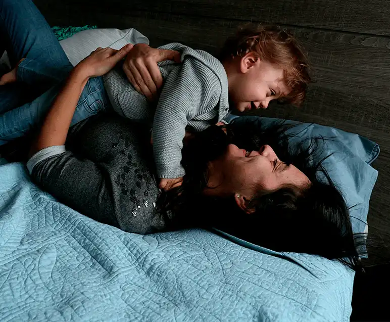 Mãe e filho brincando e rindo juntos na cama, mostrando alegria e conexão em um momento de diversão e amor familiar.