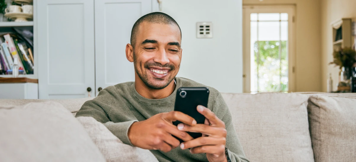 homem-sorridente-usando-celular-em-casa
